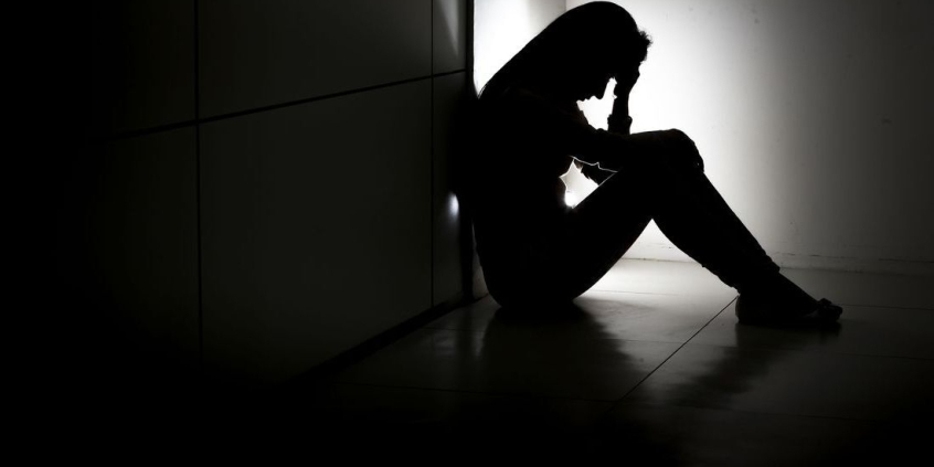 foto em negativo preto e branco mostra mulher sentada apoiando as mãos na cabeça