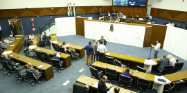 Vereadores sentados no Plenário, diante da Mesa Diretora; um parlamentar está de pé ao microfone 