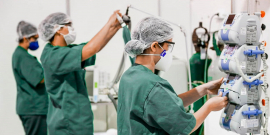 a imagem mostra três enfermeiros de pé, com jalecos verdes, operando equipamentos em UTI