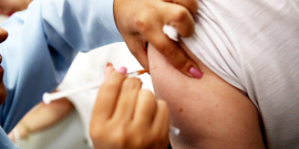Profissional aplica vacina em pessoa com uma camiseta branca