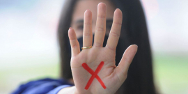 a letra X, em vermelho, na palma da mão estendida na frente do rosto de uma mulher 