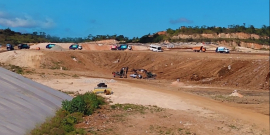 Aterro sanitário. Área de terra batida, local amplo e veículos de caçamba, entre escavadeiras e caminhões, durante o dia