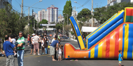 Crianças em brinquedo inflável gigante na via, ao lado de adultos que conversam livrmente