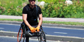 cadeirante do sexo masculino com camiseta e capacete preto e luvas amarelas transitando na rua