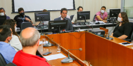 Vereador Braulio Lara (Novo) sentado à mesa com quatro pessoas. Ao fundo, seis assistentes do Legislativo. 