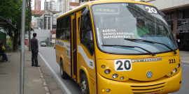 Ônibus suplementar transitando em avenida, durante o dia.