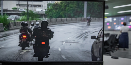 Imagem da tela co computador com motos em cima de um viaduto. Ao fundo , o Plenário onde acontece a reunião