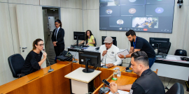 Vereadores discutem projetos no plenário. O telão atrás deles mostra videochamada com vereadores presentes virtualmente.