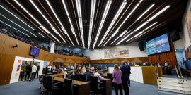 Vereadores se reúnem presencialmente na primeira reunião do Plenário da 20ª Legislatura. A foto mostra vereadores sentados e em pé, em visão lateral, bem como a mesa diretora e o telão.