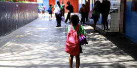 Menina é vista de costas dentro de escola usando uniforme e mochila rosa