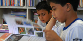 crianças com uniforme de escola fazem leitura de livro em biblioteca