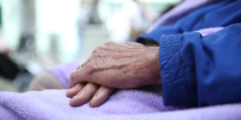 Mãos idosas sobre cobertor roxo