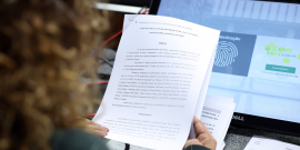 mulher de costas segura folha com texto em frente a tela de computador com imagem sobre identificação digital