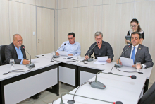 Integrantes da Comissão estão sentados à Mesa apreciando a pauta da reunião; no canto direito da foto aparece uma servidora com uma prancheta na mão