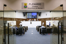 vista geral do Plenário Amynthas de Barros_vista a partir da porta de entrada. Porta de vidro aberta, em primeiro plano. Ao fundo, vereadores ocupam os seus lugares. No alto, placa indica o nome do Plenário