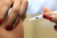 Mão de mulher aplicando vacina num braço 
