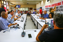 Imagem do Plenário Helvécio Arantes com vereadores sentados à mesa em formato de U. Ao fundo é possível ver as cadeiras ocupadas por movimentos populares que afixaram faixas de protestos na parede