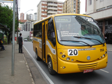 Ônibus suplementar transitando em avenida, durante o dia.