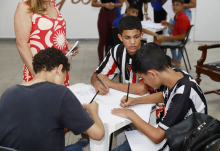 Três estudantes desenhando, sentados à mesa.