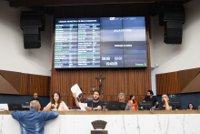 Imagem da mesa diretora. ao centro, o presidente Gabriel levanta uma folha ofício
