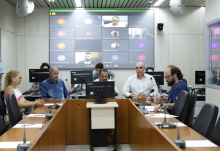 Quatro parlamentares e uma representante sindical reunidos, sentados à mesa. Ao fundo, telão exibe participação remota de representantes da Secretaria Municipal de Saúde.