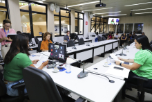 Vereadoras assentadas no Plenário Helvécio Arantes, em mesa com formato de U. O computador à frente de Loíde mostra chamada virtual e pequena plateia assiste à frente.