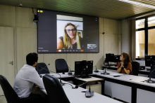 Luiza Dulci e Uner Augusto estão assentados no Plenário Helvécio Arantes. O telão à frente deles mostra Flávia Borja em chamada virtual.