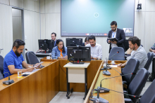 Imagem dos vereadores em reunião sentados em volta de uma mesa em formato U com um telão azul ao fundo