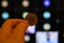 foto de uma mão segurando uma moeda de um real
