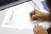 Mão de vereadora assina documento durante reunião da Comissão de Mulheres